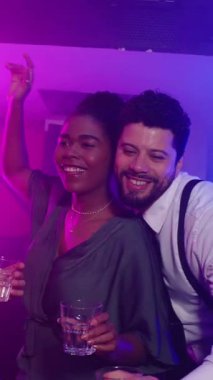 Enerjik genç yetişkinler dans ediyor, içiyor ve neon ışıkları ve titreşimli müzikle gece hayatından keyif alıyorlar.