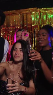 Genç kadınlar ve erkekler partiden zevk alıyor, yavaş çekimde altın bir arka plana karşı dans edip şampanya içiyorlar.