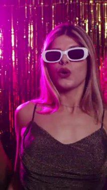 Yavaş çekimde, genç bir kadının kokteyl içip, arka planda parlak bir disko partisinde dans edişinin videosu.