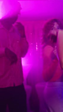 Gece kulübünde renkli ışıklar ve ağır çekimde dumanlı atmosferle dans eden enerjik kadınlar.