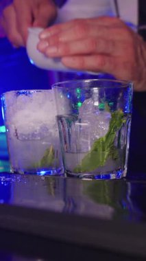 Yetenekli barmen tazeleyici kokteyller hazırlıyor, bardaklara taze naneli ezilmiş buz ve soda ekliyor, canlı bar ortamında profesyonel karışım tekniği sergiliyor.