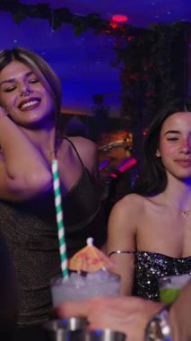 Genç kadınlar bar tezgahında gülüp konuşuyorlar, içkiden zevk alıyorlar ve hareketli bir gece kulübü atmosferinde birbirlerine eşlik ediyorlar. Video yavaş çekimde.