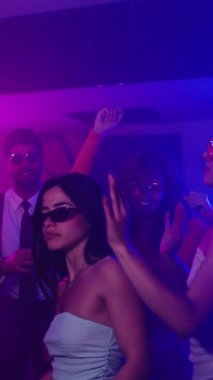 Genç insanlar loş ışıklı gece kulübünde dans ediyorlar, enerjik ritimlerle ağır çekimde hareket ediyorlar, enerjik gençliği somutlaştırıyorlar ve hafta sonu gece hayatı kutlamaları yapıyorlar.