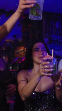 Arkadaşlar kadehlerini kaldırıyor, kadeh kaldırıyor ve neon ışıklarıyla aydınlatılan yavaş çekim bar atmosferinde neşeli bir enerjiyle gece hayatını kutluyorlar.