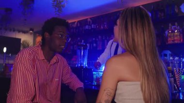 Barda sohbet eden genç çift barmen arka planda kokteylleri hazırlarken yavaş çekimde yakalandı.