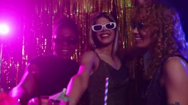 Gece kulübünde içki içen genç kadınlar. Parlayan ışıklar ve ağır çekimde altın renkli perdeler.