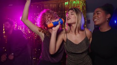 Karaokeden hoşlanan genç kadınlar, gece kulübünde kablosuz mikrofonlarla şarkı söylüyorlar, yavaş çekimde yakalandılar.