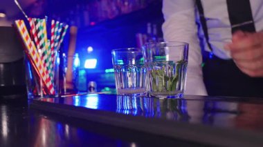 Profesyonel barmen, canlı kokteyl ile taze nane karışımını karıştırıyor. Şık bir gece kulübünde, mavi ışık altında içki hazırlıyor.