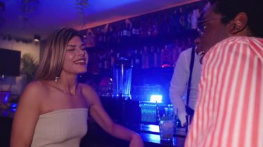 Bir kadının barda bir adamla gülüp konuştuğu ve barmenin arka planda içkileri hazırladığı yavaş çekim videosu.