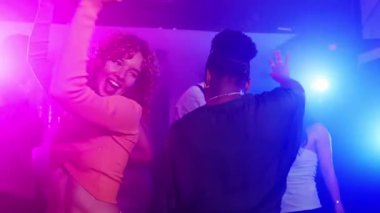 Kalabalık dans pistinde enerjik bir şekilde dans eden arkadaşlar neşeli grubu çevreleyen canlı gece kulübü ışıklarıyla ritmik müziğe geçiyorlar.
