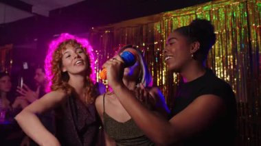 Arkadaşlar tutkulu bir şekilde karaoke söylüyor, neşe dolu bir anı paylaşıyorlar ve gece kulübünde renkli ışıklar ve altın perde altınla bağlantı kuruyorlar.