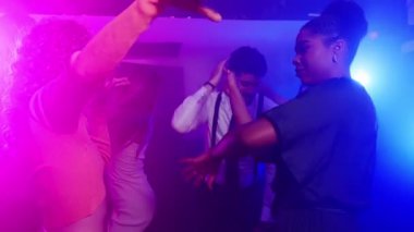 Arkadaşlar enerjik bir şekilde yavaş çekimde dans ediyor, renkli disko ışıkları altında coşkulu gece klübü kutlamalarında neşeyle hareket ediyorlar.
