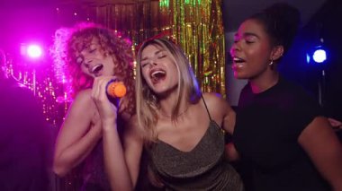 Genç kadınlar karaokeyi seviyorlar, kablosuz mikrofonla şarkı söylüyorlar, ağır çekimde birlikte eğleniyorlar.
