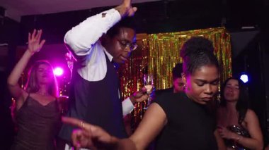 Gece kulübü sahnesinde şık Afrikalı Amerikalı arkadaşlar dans ediyor, neşe ve bağlantı paylaşıyorlar altın ışıklı ve enerjik bir atmosferle coşkulu bir kutlama yapıyorlar.