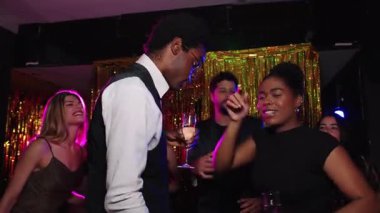 Neşeli bir grup arkadaş şenlikli anları paylaşıyor, şampanya bardaklarını tokuşturuyor ve gece kulübü kutlamalarında enerjik bir enerjiyle dans ediyor.