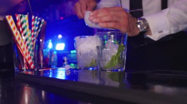 Profesyonel barmen, ezilmiş buz ve taze nane yapraklarıyla dolu bardaklara renkli malzemeler ekliyor. Yavaş çekimde miksoloji yetenekleri sergiliyor.