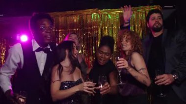 Şampanyayla kutlama yapan zarif arkadaşlar, neşeli gece hayatı partisinde dans pistinde ağır çekimde zarif bir şekilde hareket ediyorlar, neşeli bir bağ anını paylaşıyorlar.