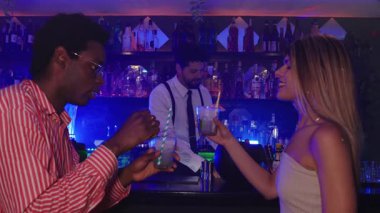 Renkli kokteyller içen genç bir çift. Trendi şehir barında samimi bir anı paylaşıyorlar. Hafif ışıklandırma ve bulanık arka plan.