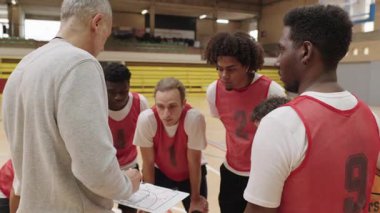 Basketbol koçu beyaz tahtaya oyun stratejisi çiziyor, oyunculara taktik planlama ve takım performans optimizasyonunda rehberlik ediyor