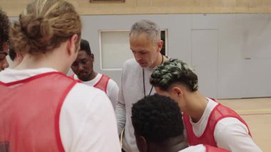 Basketbol oyuncuları stratejik mola sırasında bir araya gelerek, koçluk talimatlarını konsantre odaklanma ve takım birliği ile özümsüyorlar.