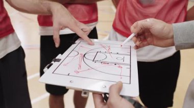Koç, basketbol stratejisini beyaz tahtayla dikkatlice açıklıyor. Yoğun takım antrenmanı sırasında oyunculara rehberlik ediyor.