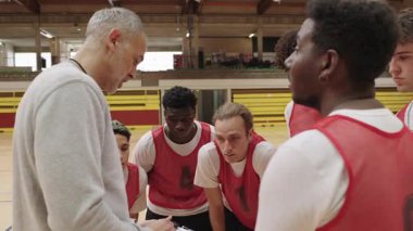 Basketbol koçu takım arkadaşlarına rehberlik eder, yoğun mola anında stratejik içgörüleri paylaşır, takım çalışmasını ön plana çıkarır ve takım spor ortamında kararlılığa odaklanır.