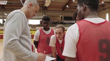 Basketbol koçu, basketbol sahasında geçirdiği yoğun zaman aralığında ilgili takım oyuncularıyla stratejik sezgilerini paylaşıyor, koçluk liderliğini ve işbirlikçi öğrenmeyi ön plana çıkarıyor.