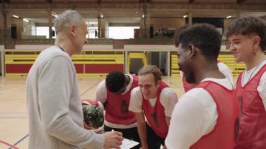 Basketbol koçu yoğun mola anında takım oyuncularıyla detaylı oyun stratejisini paylaşıyor, taktiksel tartışma ve takım motivasyonuna odaklanıyor