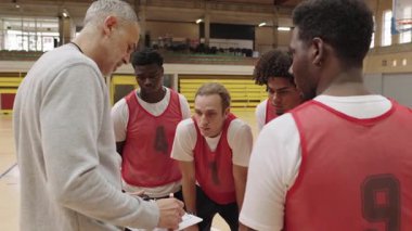 Basketbol koçu bir panoya bir oyun çiziyor ve bir süre sonra takım oyuncularına oyun stratejisini anlatıyor.