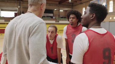 Basketbol koçu takım oyuncularıyla strateji kuruyor, spor salonunun kritik bir anında oyun taktikleri ve motivasyon sağlıyor.
