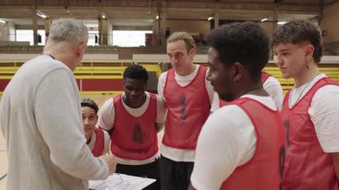 Basketbol koçu, spor salonunda antrenman yaparken takımına beyaz tahtayla oyun stratejisini anlatıyor.