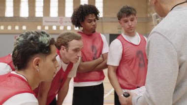 Mola sırasında basketbol koçu takımına rehberlik ediyor, oyuncuları stratejik ve motive ediyor ve spor salonunda odaklanmış liderlik ve taktiksel iletişimi var.