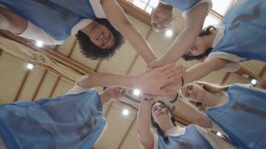 Bir grup bayan voleybol oyuncusu maçtan önce el ele tutuşarak takım ruhlarını ve birliklerini gösteriyorlar.