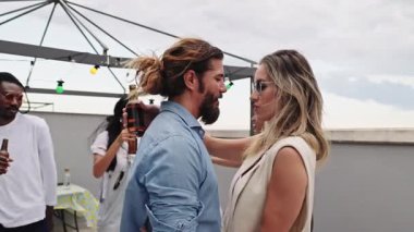 Romantik çift romantik slow dansı paylaşıyor, canlı bir akşam partisinde çatıda kucaklaşıyorlar çeşitli arkadaş grupları şehrin arka planının keyfini çıkarıyorlar.