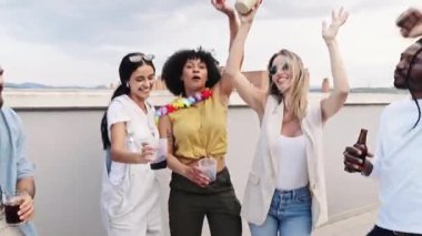 Çeşitli genç arkadaş grupları dans ediyor, içkilerini paylaşıyor ve canlı çatı katı partisinde birlikte kutlama yapıyorlar.