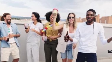 Arkadaşlar dans ederken, kokteyl içerken ve şehir çatısı üzerinde hafta sonu kutlamalarının keyfini çıkarırken şehrin arka planında neşeli anları paylaşıyorlar.
