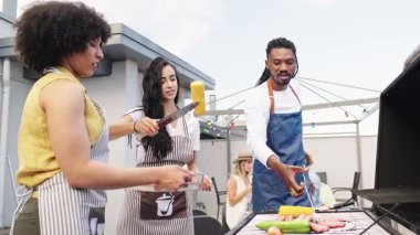 Koruyucu önlükler giyen çok ırklı arkadaşlar canlı barbekü toplantıları sırasında ızgara yemekler hazırlıyorlar, kentsel sosyal bağlar ve aşçılık keyfi sergiliyorlar.