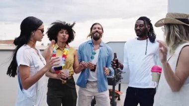 Çok kültürlü genç arkadaşlar gülüşlerini, kadeh tokuşturuşlarını ve canlı sohbetlerinin keyfini çıkarıyorlar. Gün batımı kutlamalarında şehrin arka planında.