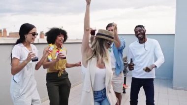 Çeşitli genç arkadaşlar neşeli anları paylaşıyor, dans ediyor ve gün batımında canlı çatı partisinde kokteyllerle kutlama yapıyorlar.