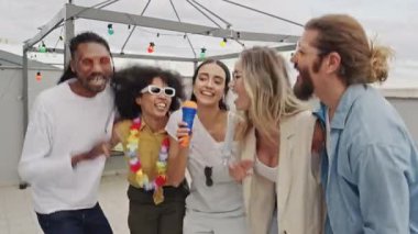 Çok ırklı arkadaşlar canlı çatı kutlamaları sırasında neşeli karaoke anları yaşıyor, kentsel ufuk çizgisi altında müzikal enerjiyi ve tasasız bağlantıyı paylaşıyorlar.