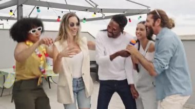 Çok ırklı arkadaşlar canlı yaz partileri sırasında renkli ışıklar ve ortak müzikal heyecanlar eşliğinde şehir çatılarında şarkı söyleyip karaoke yapıyorlar.