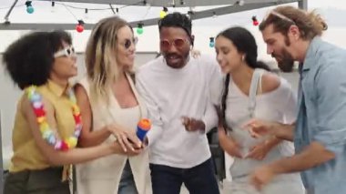 Cok uluslu arkadaslar karaoke soyluyor, yuksek bir yaz kutlamalari sirasinda sehrin ufuklarinda neşeyle dans ediyorlar.