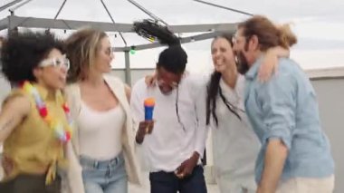 Arkadaşlar yüksek enerjili karaoke yapıyorlar, şehir çatısı toplantılarında müzik dinletisinin tadını çıkarıyorlar çarpıcı şehir manzarası arka planında, çok kültürlü grup ilişkilerini sergiliyorlar.