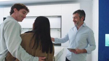 Modern bir mutfaktaki genç bir çifte ev projesinin detaylarını anlatan dijital tablet kullanan mimar