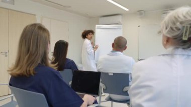 Tıp uzmanları konferans için toplanıyor, yavaş çekim profesyonel ortamında yürüyor ve stratejileri tartışıyorlar.