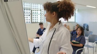 Hastane sınıfındaki sunum sırasında tıp öğrencilerine beyaz tahtada bir şey açıklayan kadın doktor.