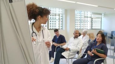 Kadın doktor, bir hastane toplantı odasında meslektaşlarına sunum yapıyor.