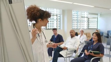 İşbirlikçi ekip toplantısında tıbbi görüşleri sunan profesyonel kadın doktor, sağlık ortamında beyaz tahtayla ilgili bilgileri paylaşıyor.