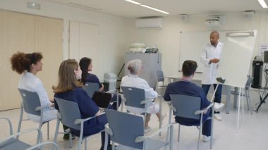 Hastane toplantı odasında bir doktorun sunumuna katılan tıp uzmanları hasta bakımı stratejilerini tartışıyor.