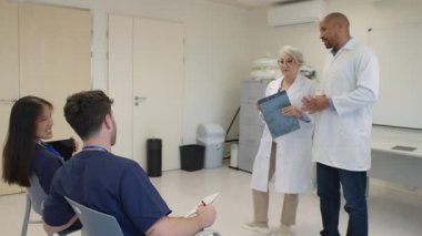 Tıbbi uzmanlar işbirliği yapıyor, hasta detaylarını inceliyor, modern hastane ortamında tedavi stratejisini tartışıyor, profesyonel danışmanlık sırasında çizelgeleri analiz ediyor.